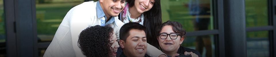 Five students sitting and standing taking a group selfie together