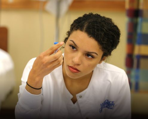 A female nursing student holds up a beaker and examines the contents.